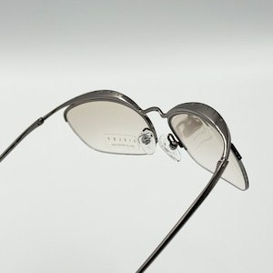 May include: A pair of silver-toned metal eyeglasses with a clear lens. The glasses have a unique design with a curved frame and a small metal detail on the side.