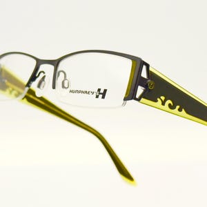 Puede incluir: Gafas negras y doradas con un diseño decorativo en las patillas. El nombre de la marca "Humphrey's H" está impreso en la montura.