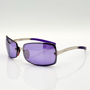 May include: Silver sunglasses with purple lenses and a silver frame. The sunglasses have a "LUMIA" logo on the side.