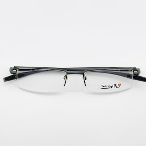May include: Black and silver-toned eyeglasses with a rectangular frame and clear lenses. The glasses have a minimalist design with a thin frame and a small logo on the right lens. The arms are dark and sleek.