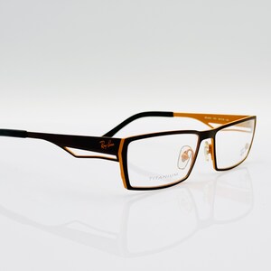 K&ouml;nnte beinhalten: Schwarze Brille mit goldfarbenem Rahmen und Titan-Gestell. Die Brille hat eine rechteckige Form und klare Gl&auml;ser.