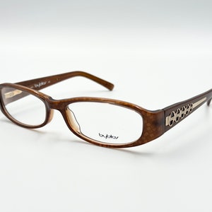 Puede incluir: Gafas de plástico marrón con un patrón de caparazón de tortuga y detalles dorados en las patillas. La marca "byblos" está impresa en la patilla derecha.