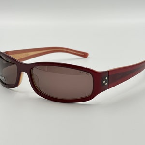 May include: Burgundy-coloured sunglasses with brown lenses and a thin, light brown stripe on the top of the frame.