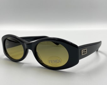 May include: Black oval-shaped sunglasses with brown lenses. The sunglasses have a Fendi logo on the side.