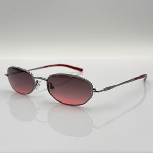 May include: Silver-framed sunglasses with a red accent on the arms and gradient pink lenses.