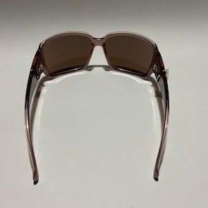 May include: A pair of brown sunglasses with a mauve frame. The sunglasses are shown from the back, with the arms of the frame extending out to the sides.