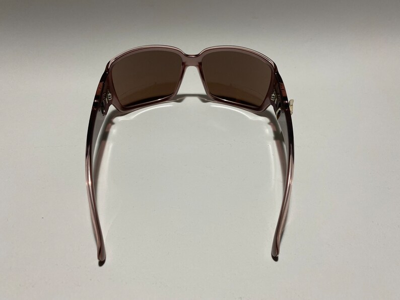 May include: A pair of brown sunglasses with a mauve frame. The sunglasses are shown from the back, with the arms of the frame extending out to the sides.