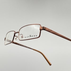 Puede incluir: Un par de gafas de metal marrón con lentes transparentes. El nombre de la marca "RICHMOND" está impreso en la montura.