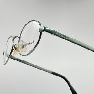 May include: A pair of silver-toned round eyeglasses with Giorgio Armani branding on the arm.