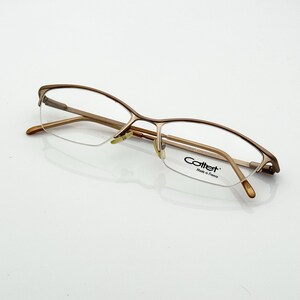 Könnte beinhalten: Braune Metallbrille mit Halbrand-Design. Die Brille hat klare Gläser und der Markenname "Cottet" ist sichtbar. Der Rahmen hat ein dünnes, filigranes Aussehen.