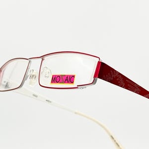 Puede incluir: Gafas de vista rectangulares de color rojo y blanco con una varilla blanca con estampado. El marco tiene una pequeña pegatina rosa con la palabra "MOSAIC" en ella.