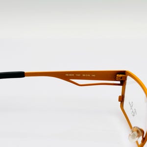K&ouml;nnte beinhalten: Orangefarbene Metallgestellbrille mit schwarzen B&uuml;geln. Der Rahmen tr&auml;gt den Text "RB 5045 1101 55 015 140", der auf der Innenseite des Rahmens aufgedruckt ist.