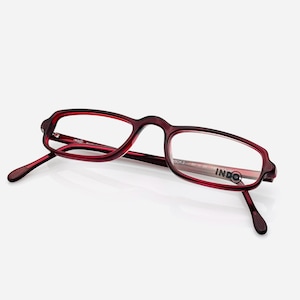 May include: A pair of maroon-colored eyeglasses with a rectangular frame and clear lenses. The glasses have a subtle, rounded design at the corners and the brand name "INDO" is visible on the lens.