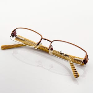 Puede incluir: Gafas de metal marrón con lentes transparentes y una varilla de color dorado. La varilla tiene el texto "Toi & moi" impreso en ella.