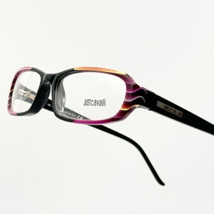 May include: Black and purple eyeglasses with a gold and orange accent on the frame. The brand name "Just Cavalli" is printed on the right lens.