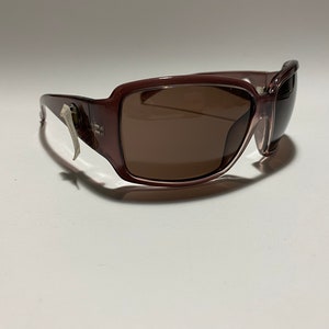 May include: A pair of brown plastic sunglasses with a silver accent on the side. The sunglasses have a rectangular shape and brown lenses.