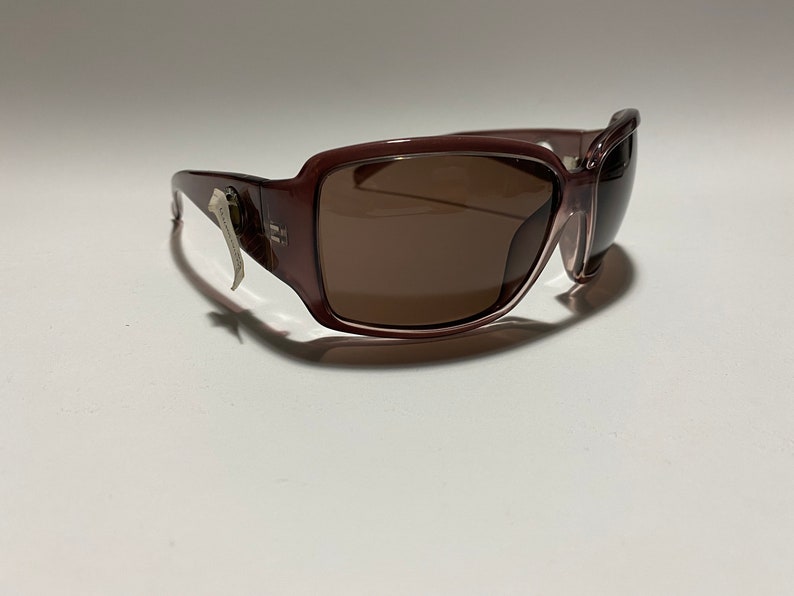 May include: A pair of brown plastic sunglasses with a silver accent on the side. The sunglasses have a rectangular shape and brown lenses.
