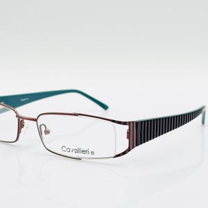 Può includere: Occhiali con montatura in metallo bordeaux e aste color teal. Le lenti sono rettangolari con un design semi-senza montatura. Le aste hanno un motivo a righe. Il marchio "Cavallieri" è stampato sulla montatura.
