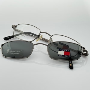 Puede incluir: Gafas rectangulares plateadas con un logotipo de Tommy Hilfiger en la lente derecha. Las gafas tienen una lente polarizada con clip magnético.