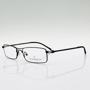 Puede incluir: Gafas rectangulares negras con montura fina. Las gafas tienen un diseño minimalista con un pequeño logotipo en la lente. La marca "Trussardi" es visible en la montura. Las gafas están sobre un fondo blanco.