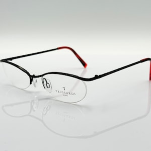 May include: Black half-rim glasses with red accents and clear lenses. The glasses have the text "TRUSSARDI EYES" on the right lens.