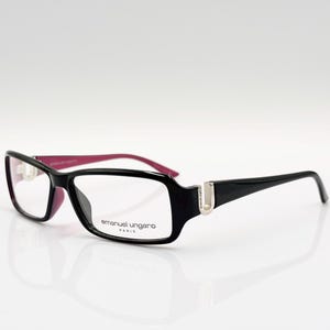 Puede incluir: Gafas negras y rosas con un logotipo U plateado en el lateral. El nombre de la marca "emanuel ungaro paris" está impreso en la montura.