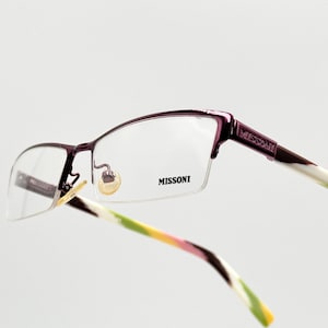 May include: Purple and white eyeglasses with a Missoni logo on the side. The glasses have a half-rim design with clear lenses.