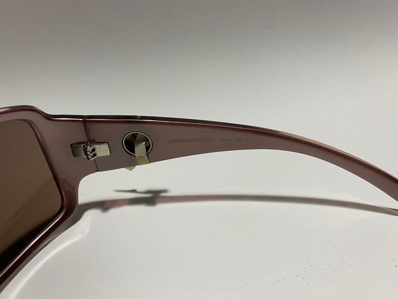 May include: Brown sunglasses with a silver hinge and the text "Versace Collection Made in Italy" on the arm.