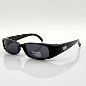 May include: Black rectangular sunglasses with dark lenses. The sunglasses have a silver label that reads "ACTION" on the right lens.