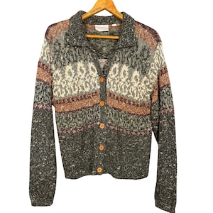 May include: A button-down cardigan sweater with a collared neckline. The sweater features a pattern of gray, brown, cream, and burgundy. The buttons are a light orange color. The sweater is hanging on a wooden hanger.