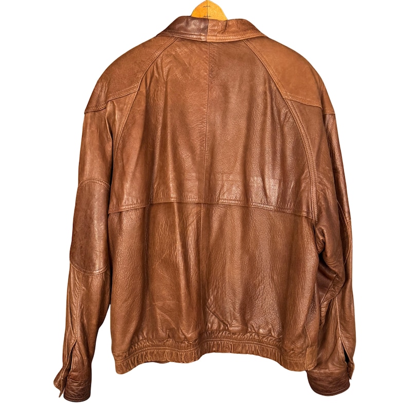 May include: A brown leather jacket with a classic design. The jacket features a collared neckline, long sleeves, and a ribbed hem. The leather has a distressed appearance, adding to its vintage appeal.