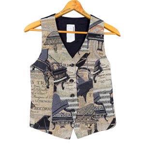 Peut inclure: Un gilet en tapisserie beige et noir avec un motif de piano et de notes de musique. Le gilet a une doublure noire et trois boutons sur le devant. Il est suspendu à un cintre en bois.
