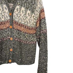 May include: A green, brown, and cream-colored cardigan sweater with a V-neck and wooden buttons. The sweater features a textured knit design with horizontal stripes and geometric patterns. The long-sleeved sweater is a cozy garment.