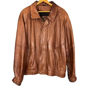 May include: A brown leather jacket with a collared neckline and a button closure. The jacket has two front pockets and a zipper closure. The leather appears to be worn and has a vintage look. The jacket is a medium size.