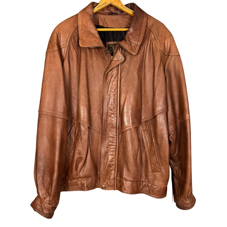 May include: A brown leather jacket with a collared neckline and a button closure. The jacket has two front pockets and a zipper closure. The leather appears to be worn and has a vintage look. The jacket is a medium size.