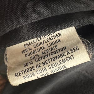 May include: Close-up of a fabric tag with text in English and French. The tag reads "SHELL/EXTERIOR 100% CUIR/LEATHER DOUBLURE/LINING 50% ACETATE 50% COTON/COTTON METHODE DE NETTOYAGE A SEC POUR CUIR SEULEMENT A VOS RISQUE."