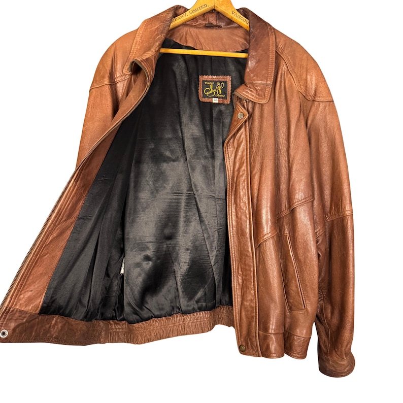 May include: A brown leather jacket with a black interior lining. The jacket has a zipper closure, a collar, and pockets. The jacket is a medium size.
