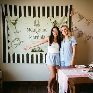 May include: A large rectangular wall tapestry featuring a light green center with a scalloped border, dark green and white vertical stripes, and the text Mountains & Martinis, Jordyn's Bachelorette, with illustrations of a martini, cowboy hat, and mountains.