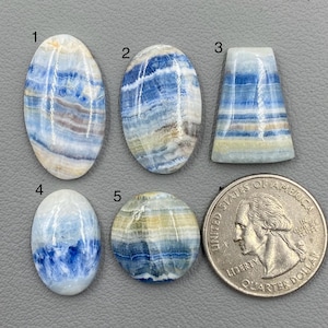 May include: Five polished gemstones in various shapes and sizes, showcasing blue, white, and tan color patterns. A U.S. quarter coin is included for size comparison. The gemstones are numbered 1 through 5.
