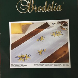 Peut inclure: Un chemin de table en damassé blanc avec un motif brodé de fleurs de mimosa jaunes. Le chemin de table mesure 40 cm sur 100 cm. Le motif de broderie s'appelle "Les mimosas" et la référence est 393.