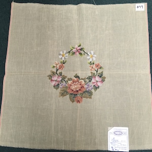 May include: Beige canvas needlepoint kit with a floral design featuring a wreath of pink, white, and purple flowers. The kit includes a label with the text "$99".