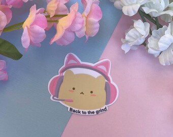 Könnte beinhalten: Ein rosa-weißer Aufkleber mit einer Comic-Katze, die einen rosa Kopfhörer trägt. Der Text "Back to the grind" befindet sich unter der Katze.