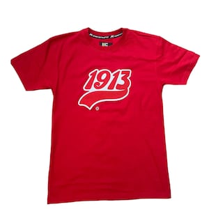 May include: Red short-sleeved t-shirt with a white and red graphic of the number "1913" in a retro baseball style font. The text "JIC STAND OUT/W/STYLE JIC STAND OUT" is printed on the collar.