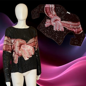 May include: A black sequined top with a pink and burgundy bow design. The bow is made of sequins and has a 3D effect.