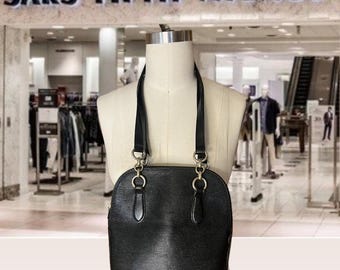 May include: A black leather handbag with gold hardware and a top handle. The bag has a textured finish and is displayed on a mannequin in a department store.