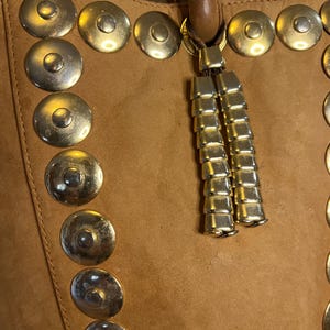 May include: A brown leather tote bag with gold metal accents and a tassel. The bag has a row of round metal studs down the side.