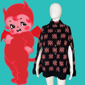 May include: A black knitted cape with a red and white geometric pattern. The cape has a high collar and button closure.