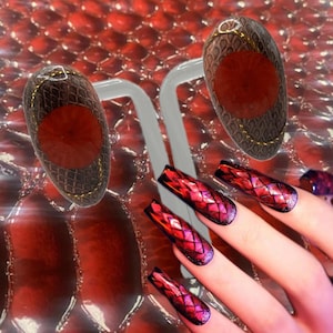 May include: An image showcasing nail art with a reptile skin theme. The nails feature a red and purple scale design. Two nail art displays are shown with a brown reptile skin pattern and a red center, accented with gold trim.