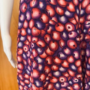 Peut inclure: Un v&ecirc;tement &agrave; motif de cerises. Le tissu pr&eacute;sente un motif r&eacute;p&eacute;t&eacute; de cerises rouges, violettes et blanches. Les cerises ont une apparence r&eacute;aliste avec des reflets et des ombres, cr&eacute;ant un aspect textur&eacute;. Le v&ecirc;tement semble &ecirc;tre une jupe ou une robe.