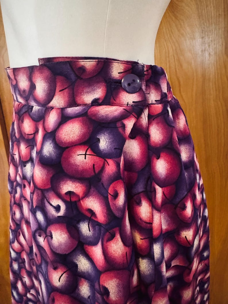Peut inclure: Jupe taille haute avec un imprim&eacute; cerise vif dans les tons de rouge, violet et blanc. La jupe a une fermeture boutonn&eacute;e et un design pliss&eacute;. Le tissu est une mati&egrave;re douce.